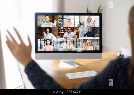 Virtual conference, online meeting. Business woman using computer app for communicating with many people at same time together. Back view in office. Video call with diverse employees Stock Photo