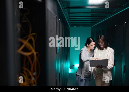 Wide angle portrait of two female IT engineers setting up server network while working in data center, copy space Stock Photo