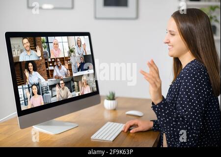 Virtual conference, online meeting. Business woman using computer app for communicating with many people at same time together. Back view in office. Video call with diverse employees Stock Photo