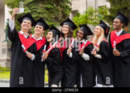 Happy graduates taking selfie together at university campus, using smartphone Stock Photo