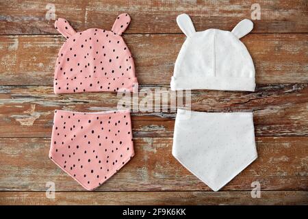baby hats with ears and bibs on wooden table Stock Photo