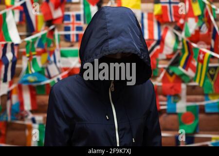 Man in a jacket with a hood against the background of a wall with flags of different states. Stock Photo