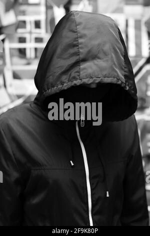 Man in a jacket with a hood against the background of a wall with flags of different states. black and white Stock Photo