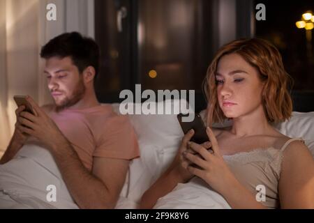 couple using smartphones in bed at night at home Stock Photo