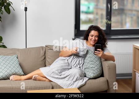 woman with smartphone drinking coffee at home Stock Photo