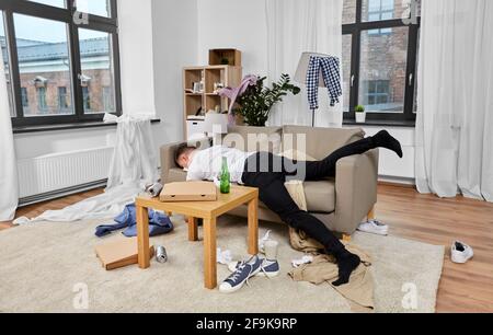 drunk man sleeping on sofa in messy room at home Stock Photo