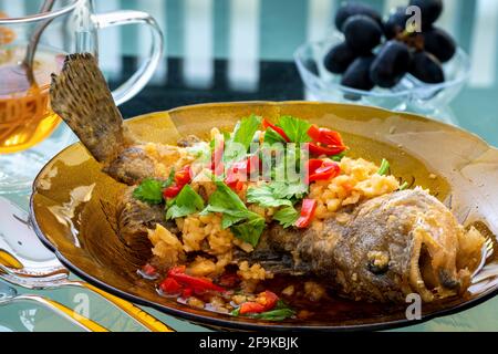 Fried grouper fish on a brown glass plate topped with condiments, Chinese cooking in Malaysia Stock Photo