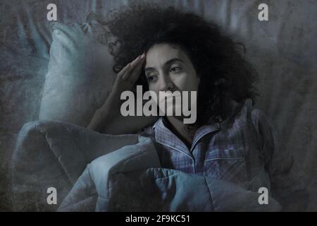 dark and edgy portrait of depressed and sleepless latin woman lying worried and awake on bed at night suffering insomnia and depression problem Stock Photo