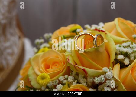 Two gold rings placed on a bouquet of yellow roses. Wedding ornament. Stock Photo