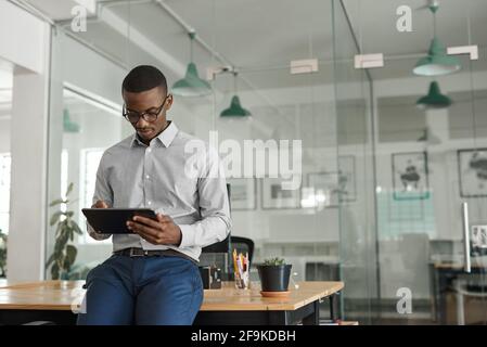 African businessman leaning on an office desk using a tablet Stock Photo