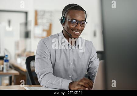 Smiling African businessman talking on a headset and using a laptop Stock Photo