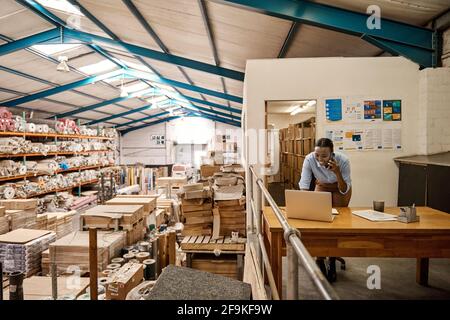 Smiling African woman talking on the phone at her warehouse desk Stock Photo