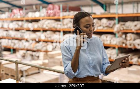 African woman with a tablet talking on a phone in a warehouse Stock Photo