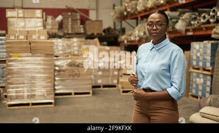 Confident young African woman holding a clipboard in a large warehouse Stock Photo