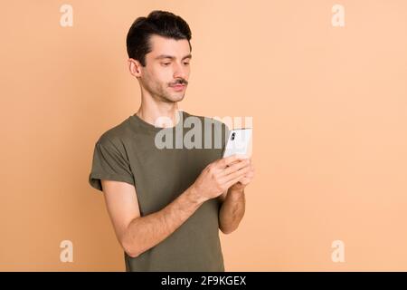 Photo portrait of man keeping mobile phone using app reading news serious isolated on pastel beige color background Stock Photo