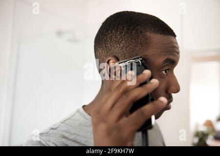 Young African man trimming his hair in his bathroom Stock Photo