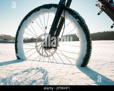 Close up of bicycle wheel on white snow. Cycling in extreme winter conditions concept and winter tyres. Stock Photo