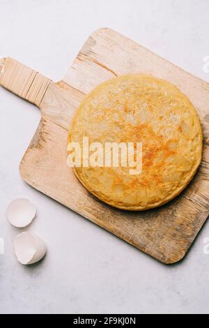 Aerial view of a potato omelet on a retro wooden table and an eggshell on a white marble background Stock Photo