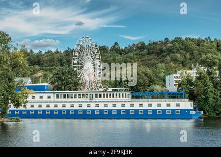 Large tourist boat with restaurant anchoring on Vltava River, ferris wheel in background, Prague, Czech republic.City excursion on boat.Tourist Stock Photo