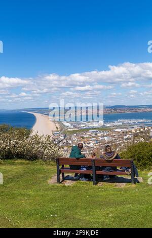 Family on bench enjoying views of Chesil Bank beach and Fortuneswell, Isle of Portland from Portland Heights, Portland, Weymouth Dorset, UK in April Stock Photo
