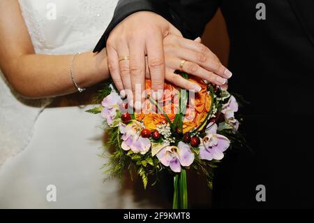 Gold rings on the joined hands of the newlyweds on the bride's bouquet. Stock Photo