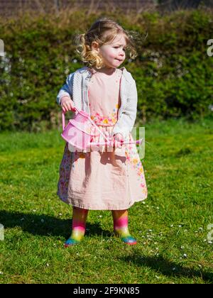Toddler in a dress with wellington boots watering daisies, UK Stock Photo