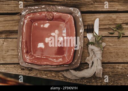 Beautiful table setting, square plates of different sizes lie on top of each other, next to it lies a fork with a knife rewound with a napkin, minimal Stock Photo