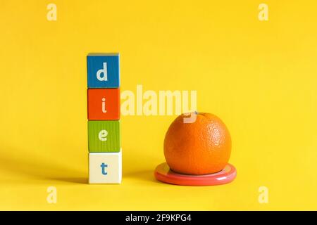 Orange on stand of pink plastic ring and word DIET made from colored wooden blocks. Painted cubes with letters are arranged vertically Stock Photo