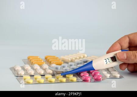 Different medicines: tablets, pills in blister pack, medications drugs and thermometer in woman's hand. Electronic thermometer Stock Photo