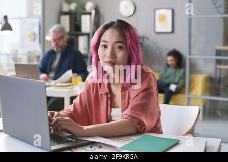 Portrait of Asian young woman sitting at the table and typing on laptop at office Stock Photo