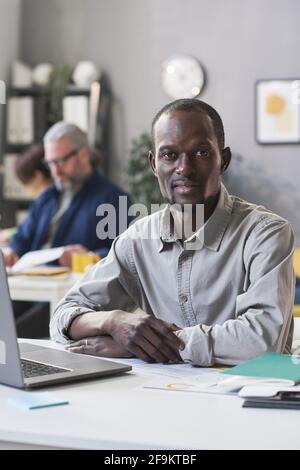 Portrait of African young man looking at camera while sitting at the table with laptop Stock Photo