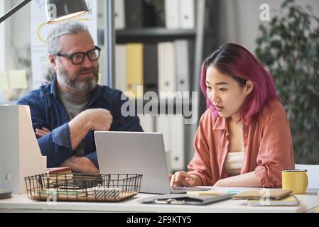 Asian young student working on laptop while sitting at the table together with her teacher Stock Photo