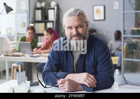Portrait of confident mature leader sitting at the table at office and looking at camera Stock Photo