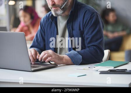 Close-up of bearded mature man typing on laptop while sitting at his workplace and working online Stock Photo