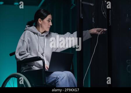 Side view portrait of disabled woman in wheelchair working with supercomputer network in server room, accessible job concept, copy space Stock Photo