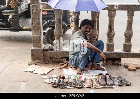 Mysuru, Karnataka, India - January 2019: A street cobbler sitting under an umbrella on the pavement in the city of Mysore. Stock Photo