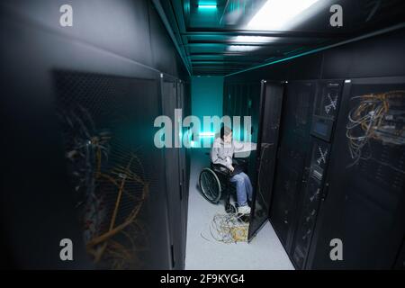Wide angle portrait of disabled woman in wheelchair working with supercomputer network in server room, accessible job concept, copy space Stock Photo
