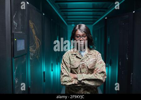 Waist up portrait of tough African-American woman looking at camera while standing in server room with futuristic background, copy space Stock Photo
