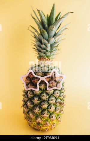 Travel and vacation concept with pineapple wearing sunglasses. Pink glasses in form of star. Relaxation on the sea. Yellow background Stock Photo