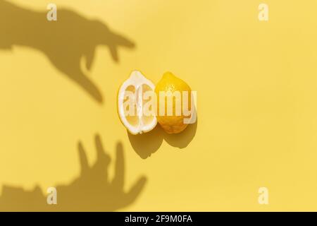 Two halved cuts of lemon with shadow from hand on yellow background. Healthy eating, travel or vacation concept Stock Photo