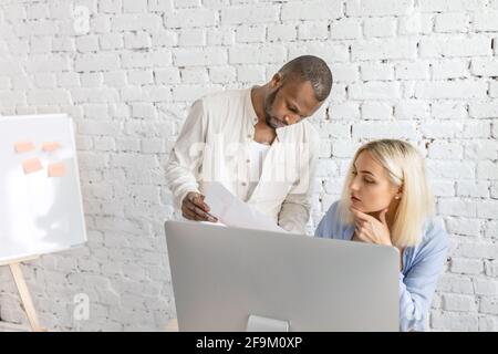 Focused serious employees learning financial graphs, working on important project. Multiracial coworkers discussing ideas for business strategy, using Stock Photo
