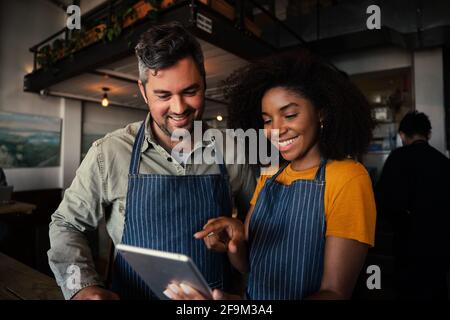 Waiter and waitress scrolling on tablet choosing menu options for customer in trendy cafe  Stock Photo