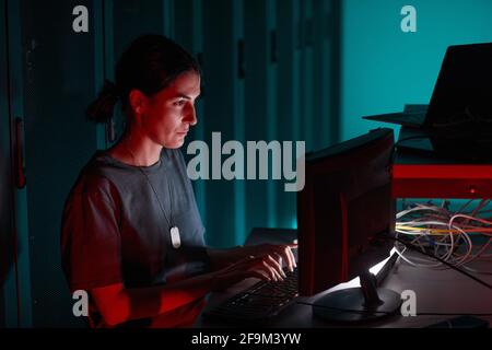 Side view portrait of female IT engineer using computer while working in server room lit by red light, copy space Stock Photo