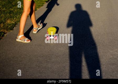 Defocus little child with penny skateboard on path in park. Boy and girl rides a penny board in sunshine day. Outdoor lifestyle picture on a sunny sum Stock Photo