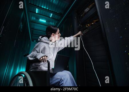 Low angle portrait of disabled woman in wheelchair working with supercomputer network in server room, accessible job concept, copy space Stock Photo