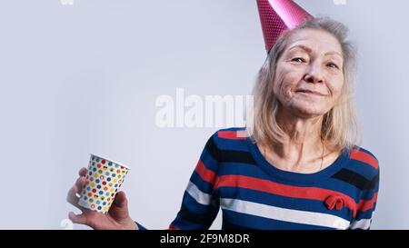 Happy elderly woman with party hat and cup of drink dancing indoors. High quality photo Stock Photo
