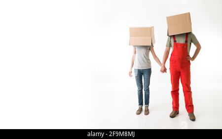 young couple with cardboard boxes on their heads, holding hands, on white background Stock Photo