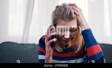 Old woman using smartphone to make phone call. Receiving bad news. High quality photo Stock Photo