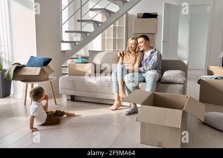 Happy family new home owners with child relaxing on sofa on moving day. Stock Photo
