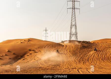Few dune buggies driving up the sand dune in the desert, with electrical towers in the background, sunset, Fossil Rock, Sharjah, United Arab Emirates. Stock Photo